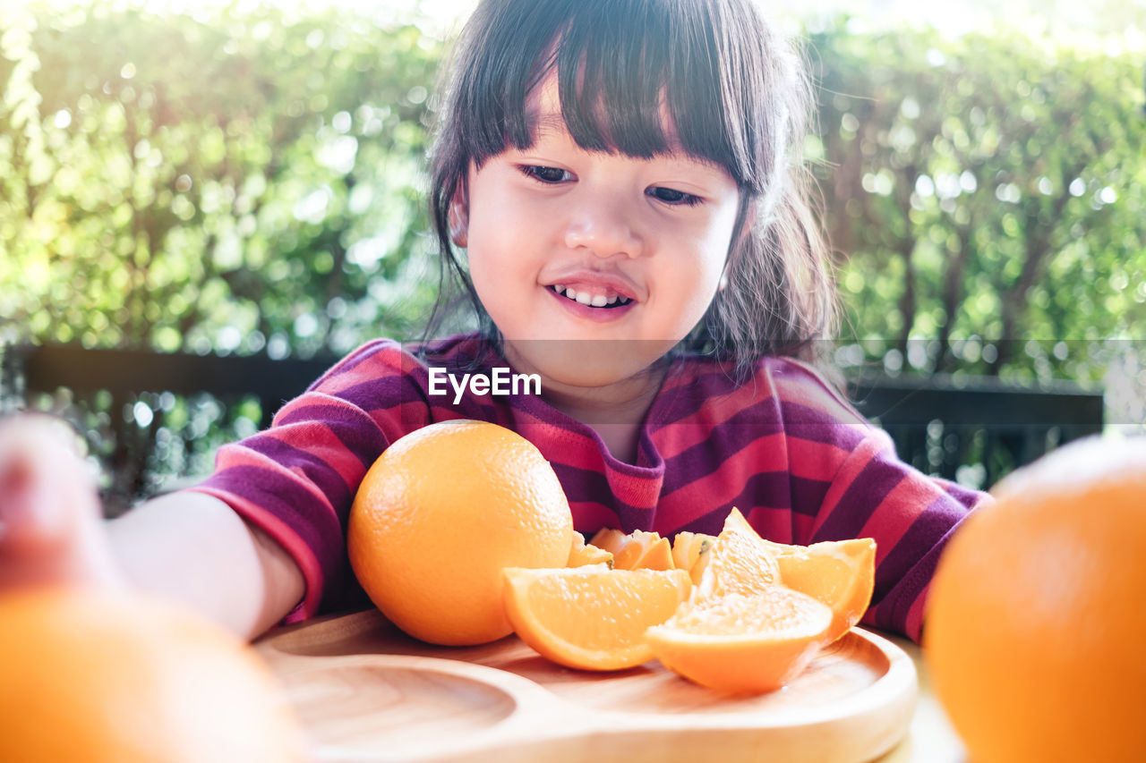 Close-up of smiling girl sitting with oranges in plate on table