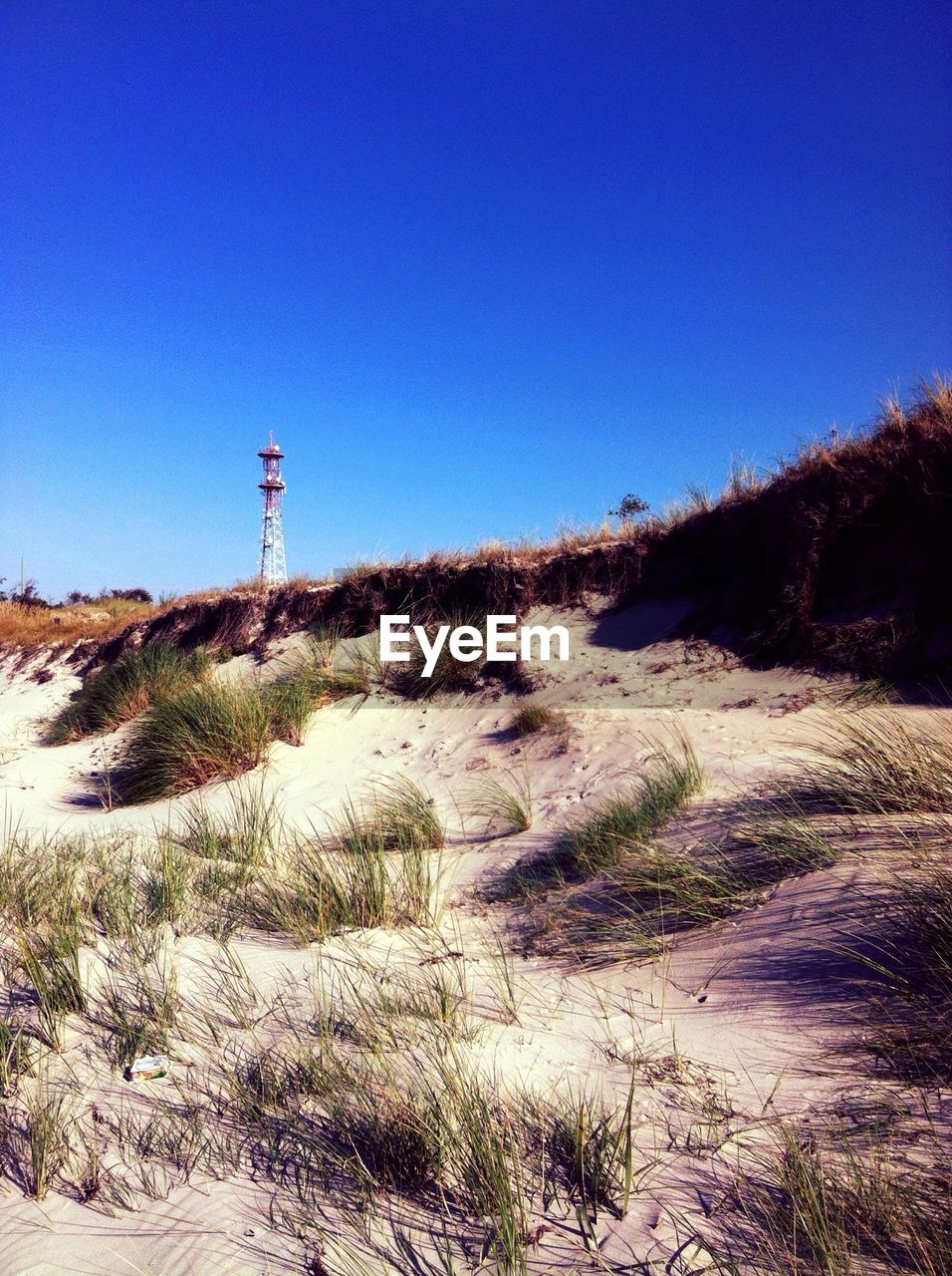 Distance shot of lighthouse on beach against clear blue sky