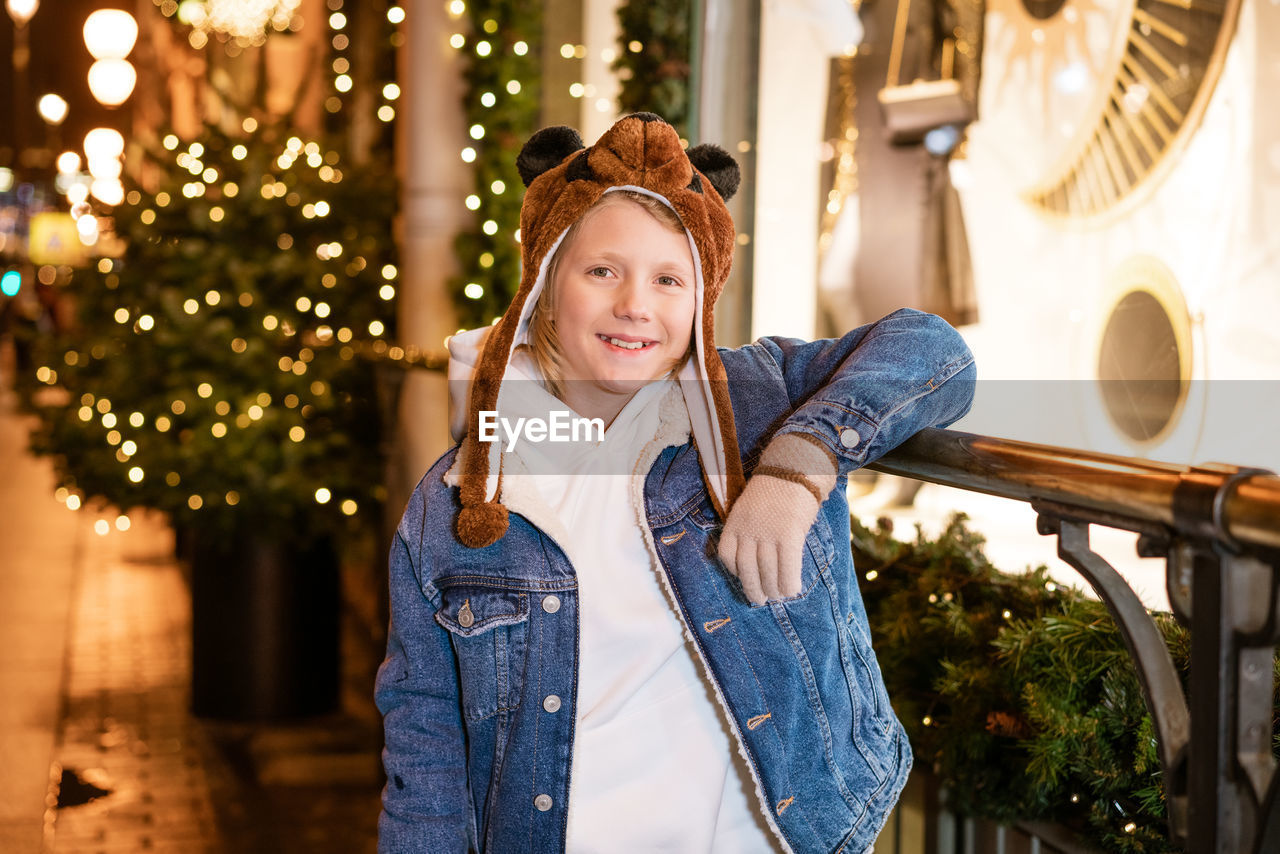 A boy smiles on the street in the evening at a shop window, a festive garland