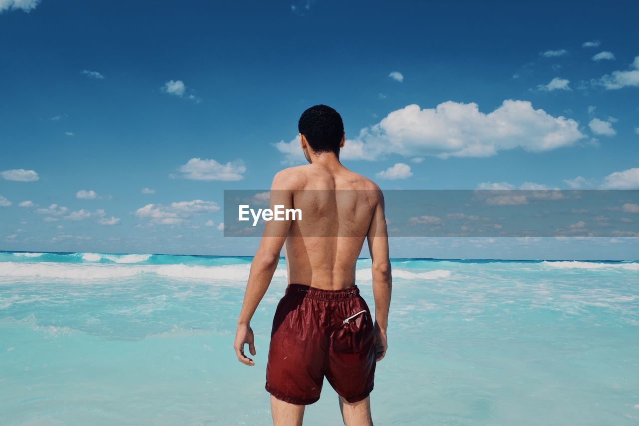 Rear view of shirtless man standing at beach