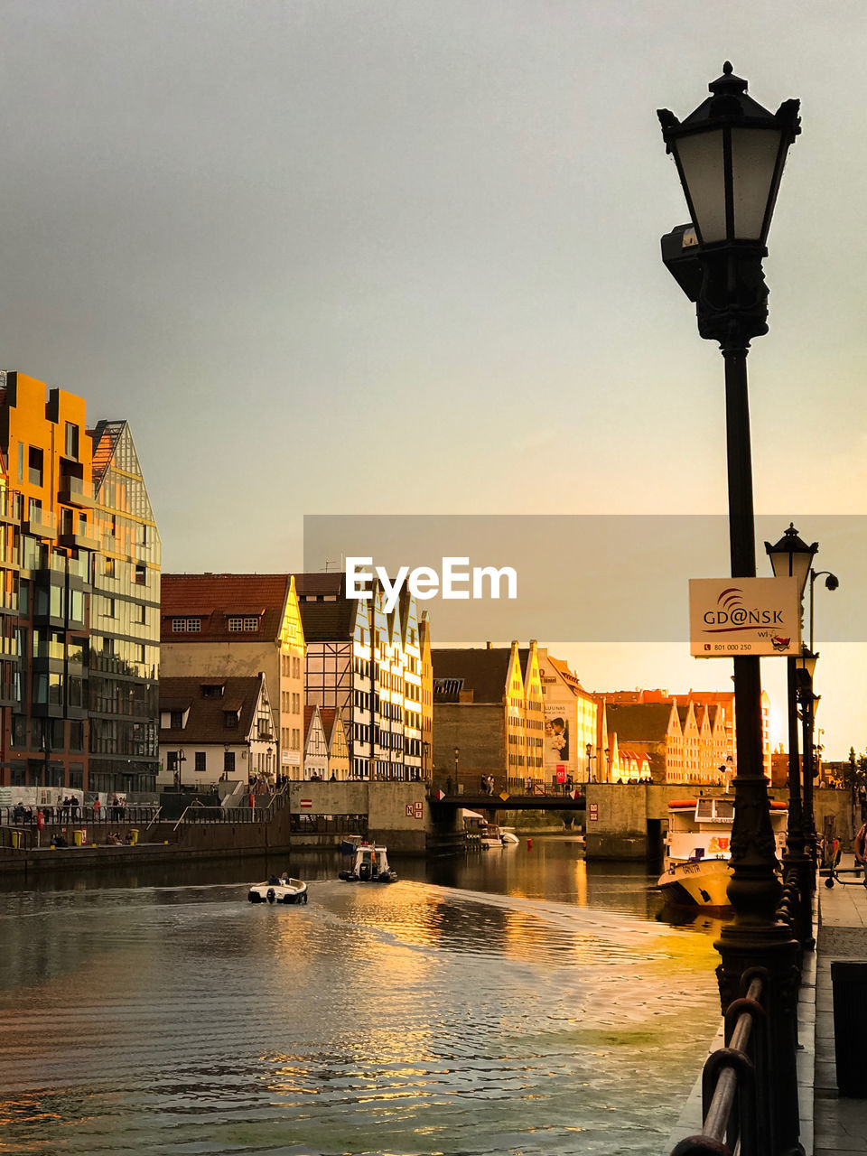 STREET LIGHT BY RIVER AGAINST BUILDINGS AT DUSK