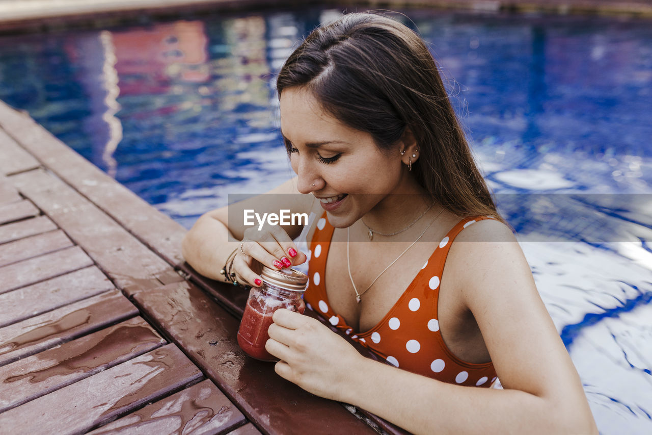 YOUNG WOMAN LOOKING AWAY WHILE SITTING ON SHORE