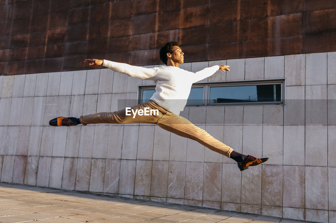 Happy male dancer doing grand jeté against building