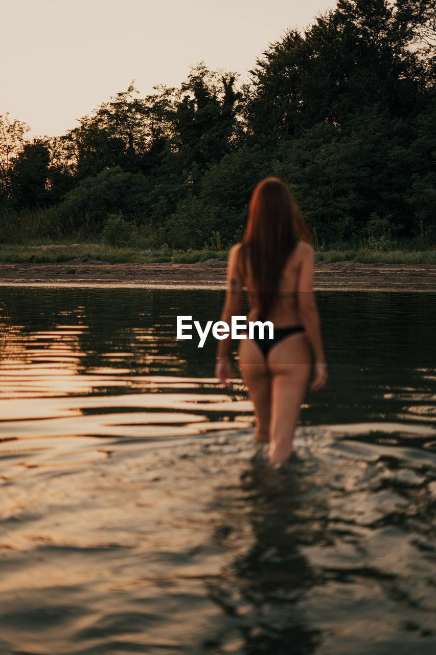 REAR VIEW OF WOMAN STANDING ON LAKE AGAINST SKY