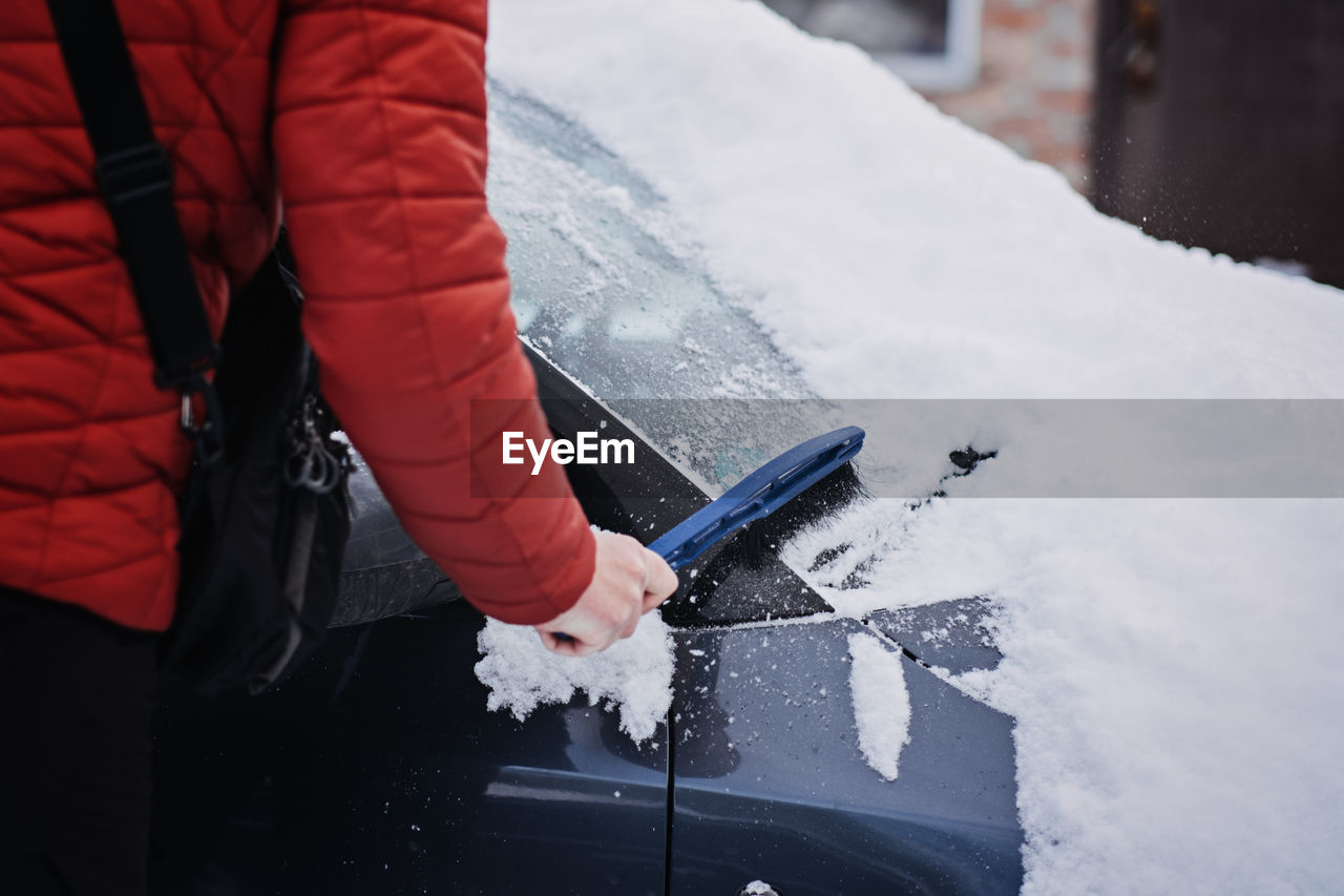 Man cleaning car from snow and ice with brush and scraper tool during snowfall. winter emergency