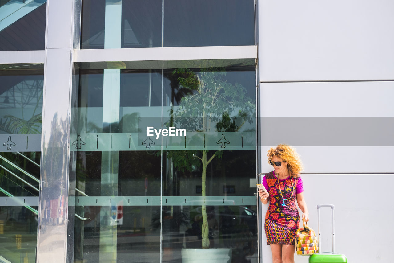 Woman using mobile phone while standing against building