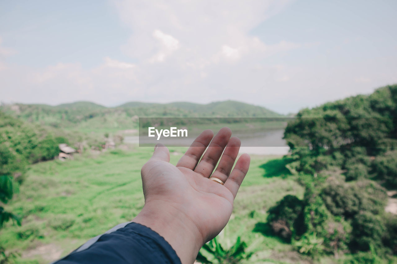 Close-up of person gesturing over land against sky