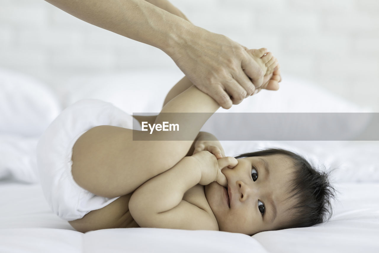 Cropped hand of mother stretching baby on bed at home