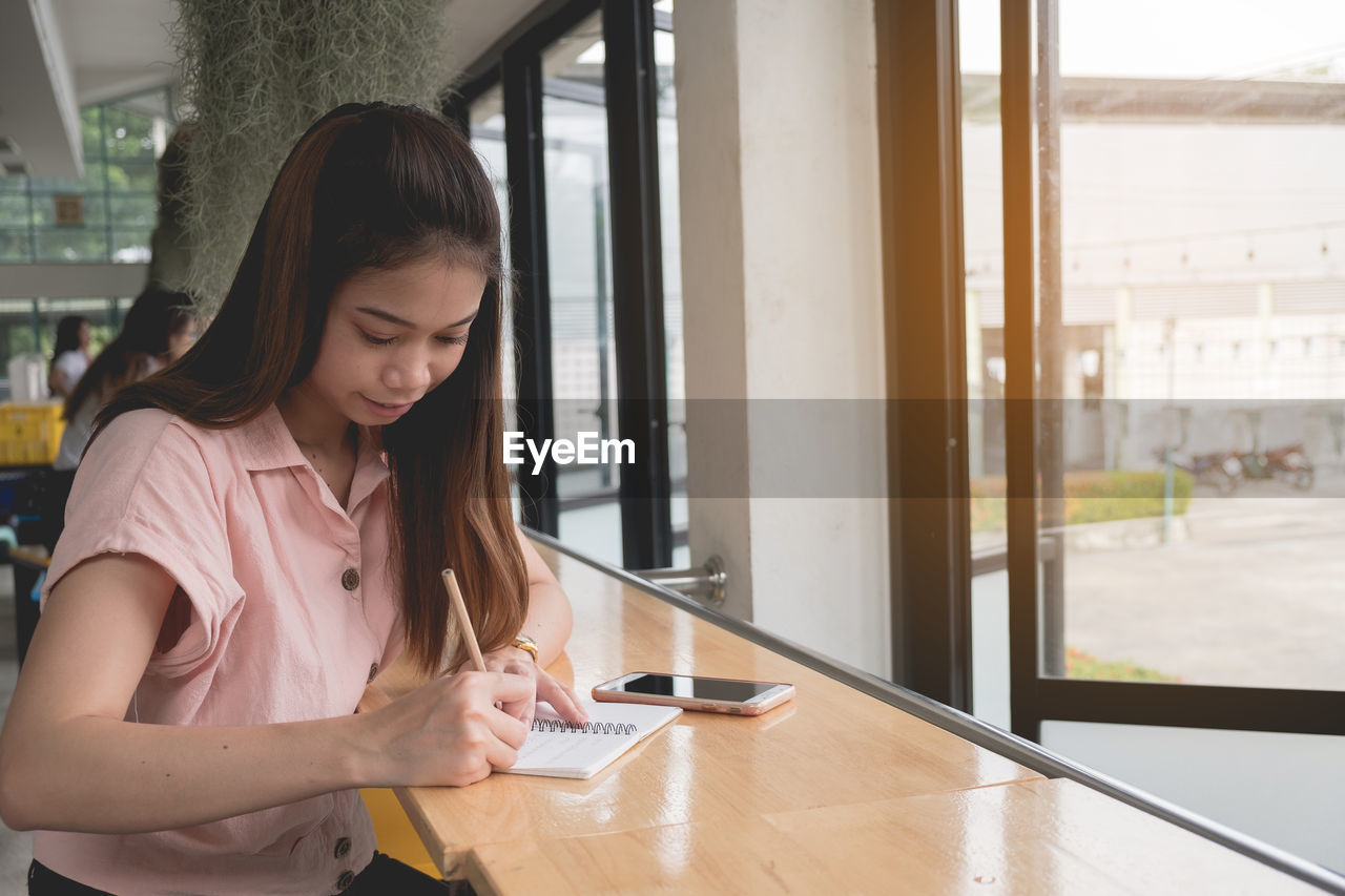 Young woman writing on book while sitting in cafe