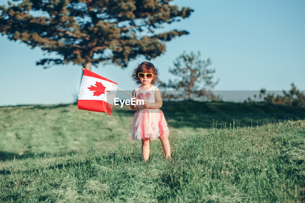 Girl holding canadian flag while standing on grass against sky