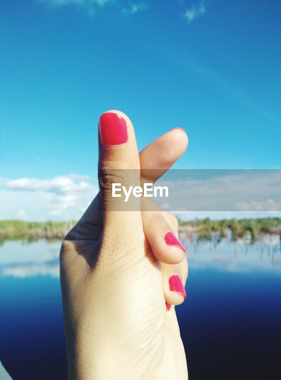 Close-up of woman hand over water against sky