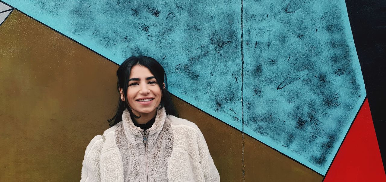 Portrait of smiling woman standing against wall