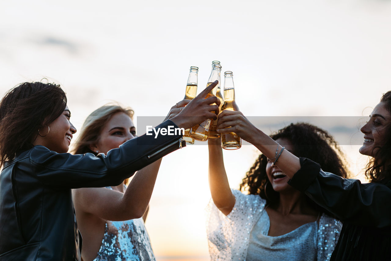 Happy friends holding beer bottle against sky