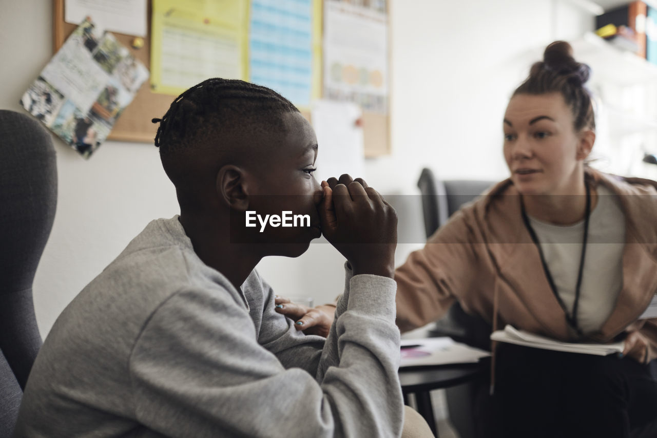 Depressed male student listening to advice from mental heath professional in school office