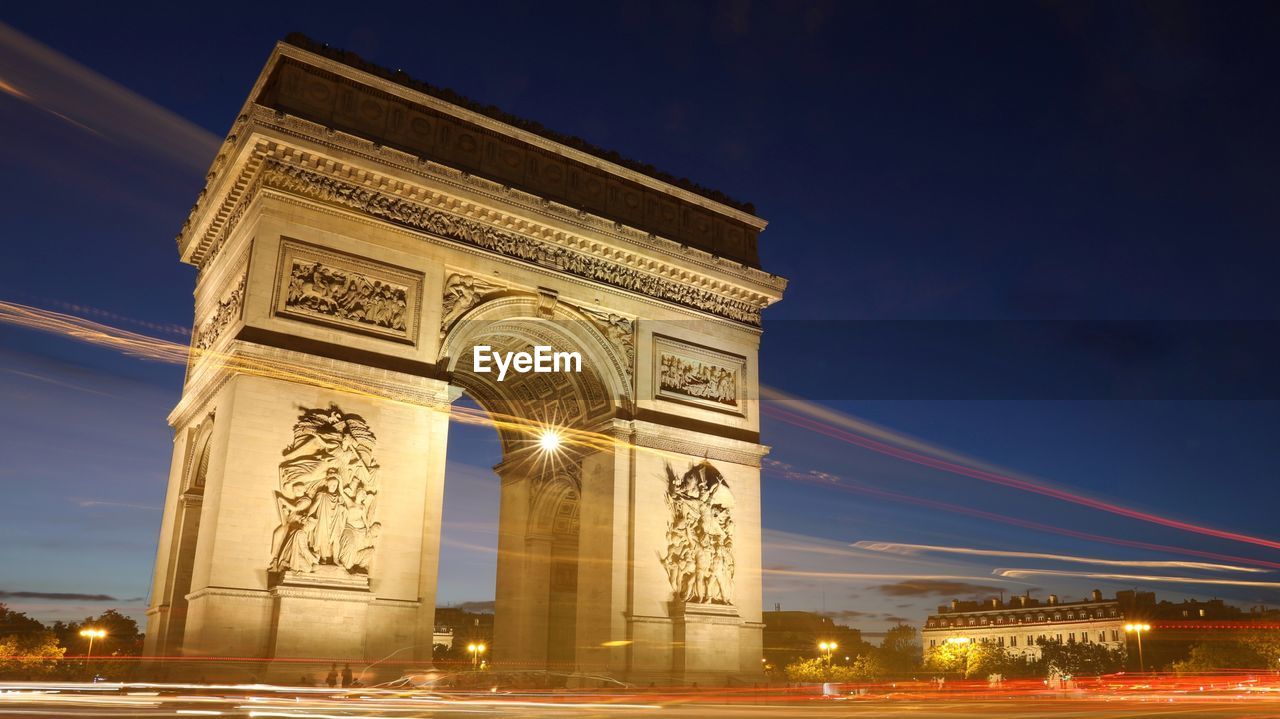 Light trails by arc de triomphe in city at night