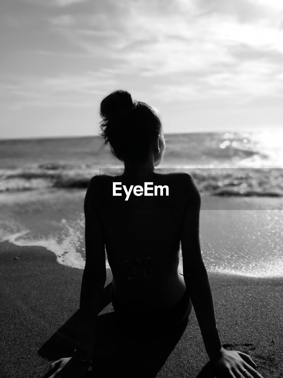 Woman sitting on beach against sky