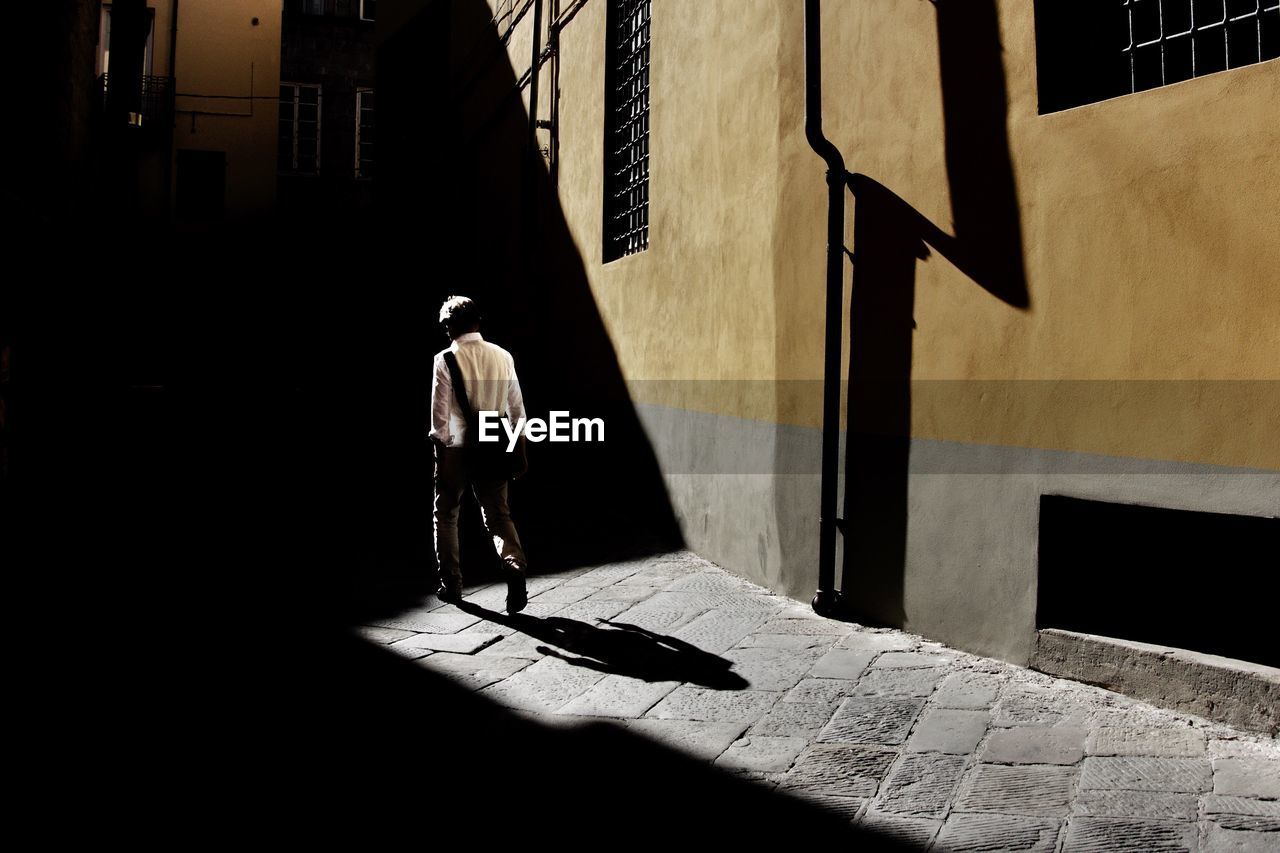 Rear view of man walking on footpath against building