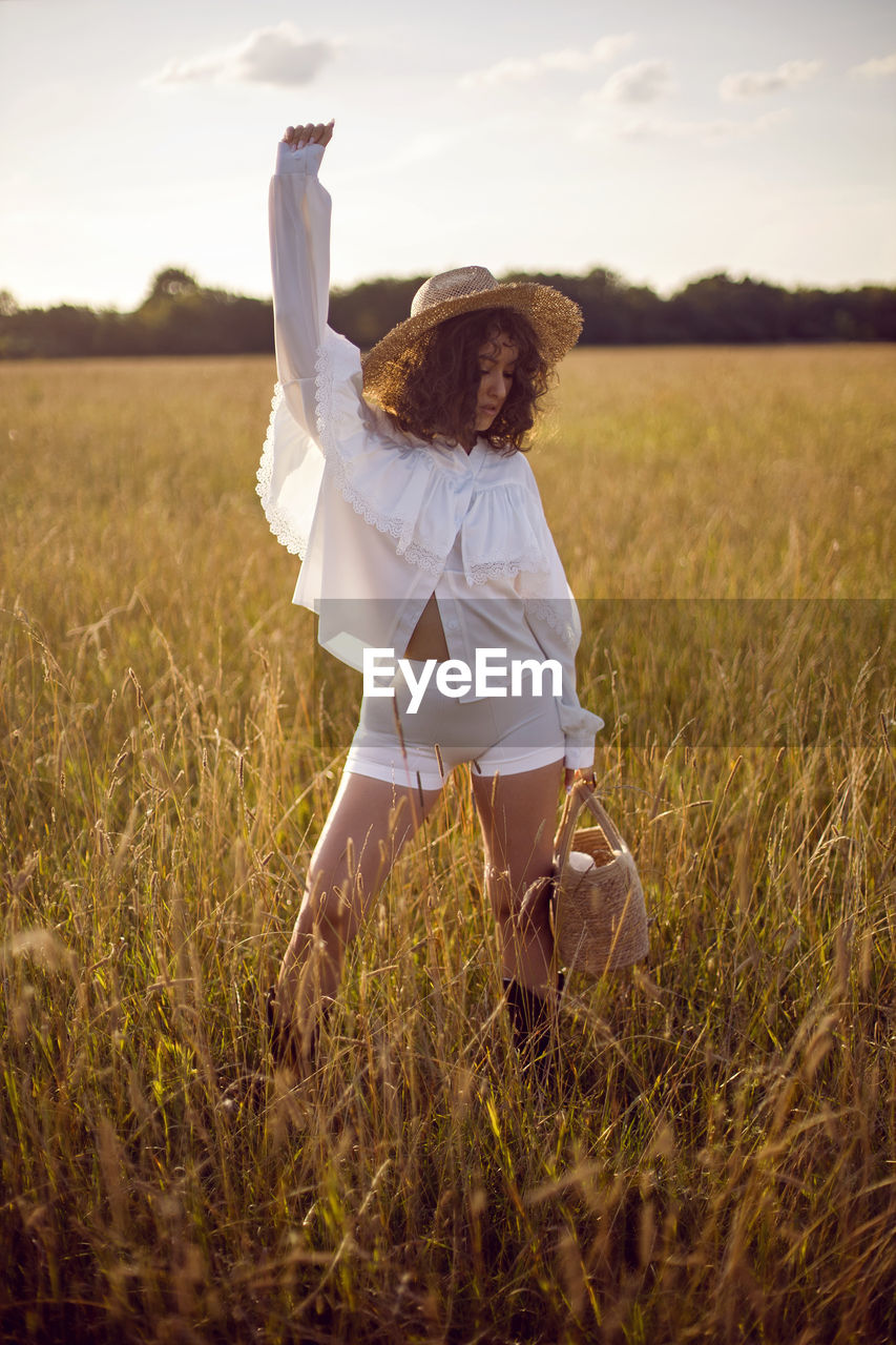 Fashion portrait of a curly-haired woman in white clothes and in a wicker hat and with a basket