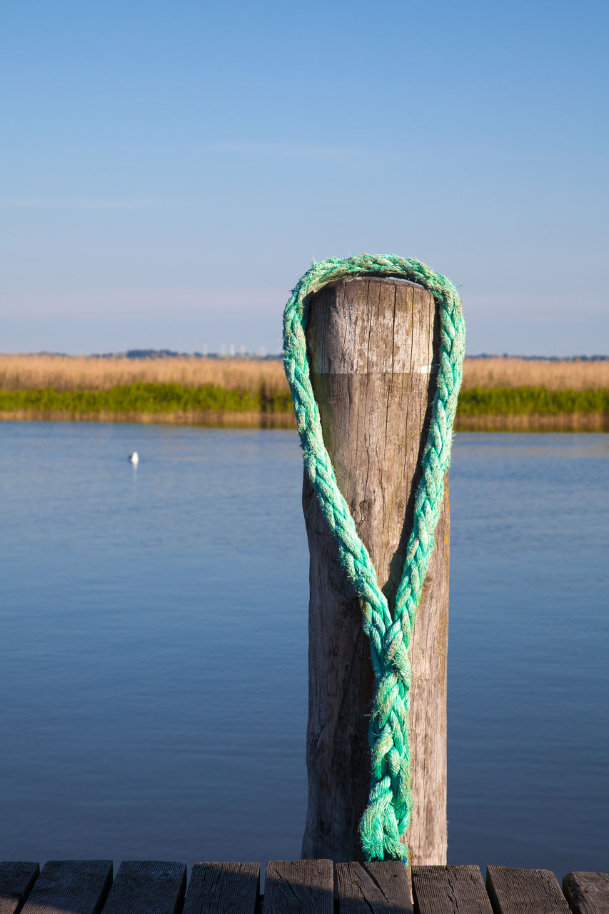 WOODEN POST BY LAKE AGAINST SKY