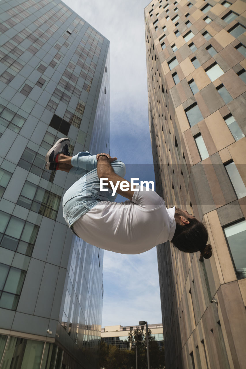 Young man practicing somersault against building in city