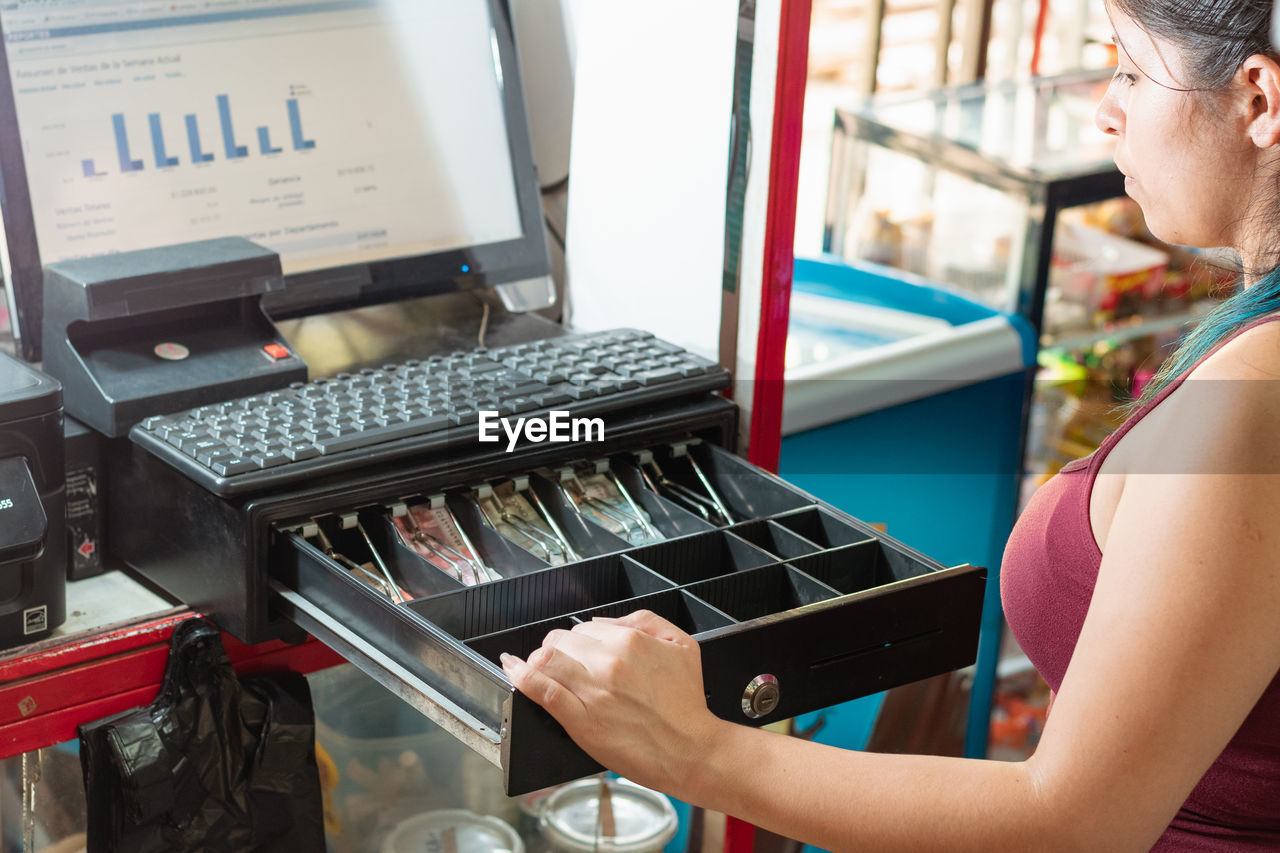 Latina woman looking disappointed at the cash register of her business to see how much money 