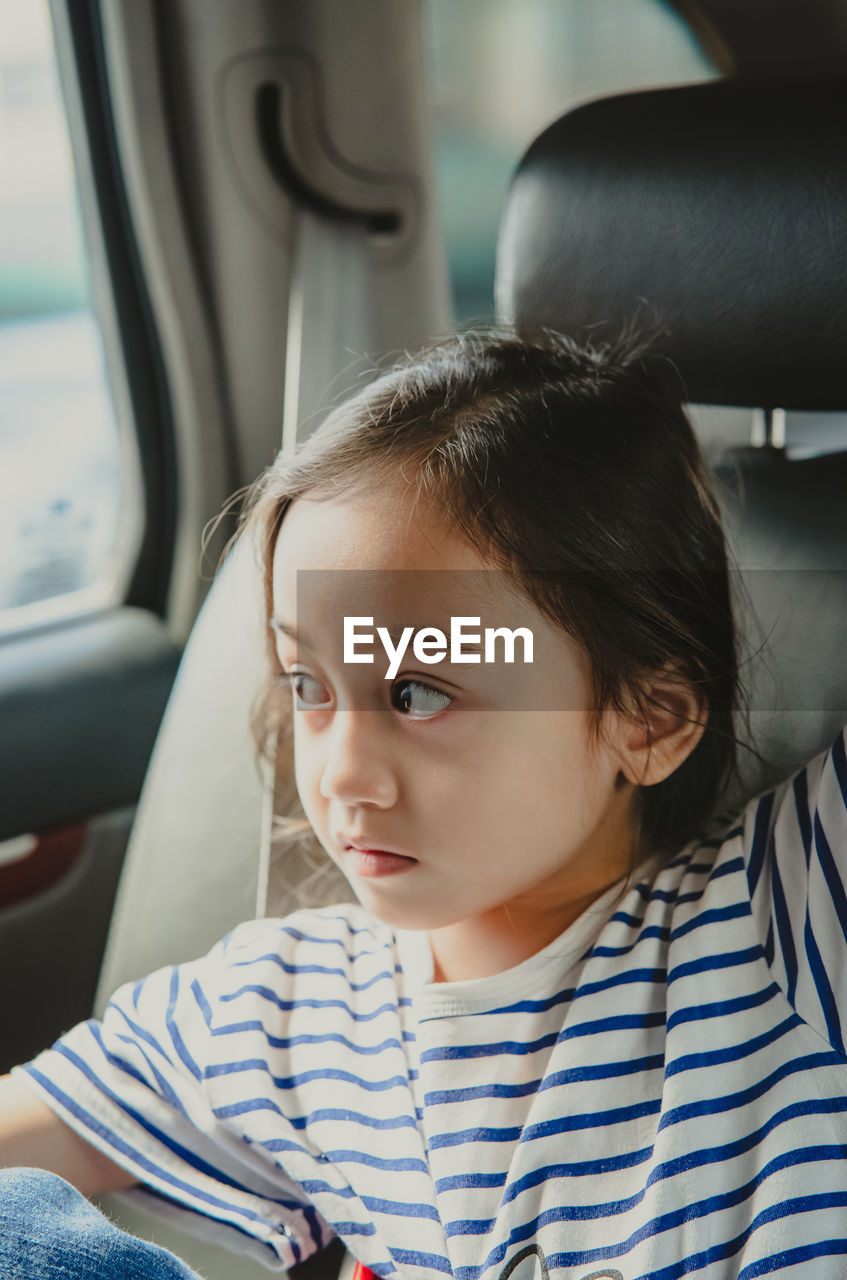 Young little girl enjoying the trip in back seat looking out the window of the car