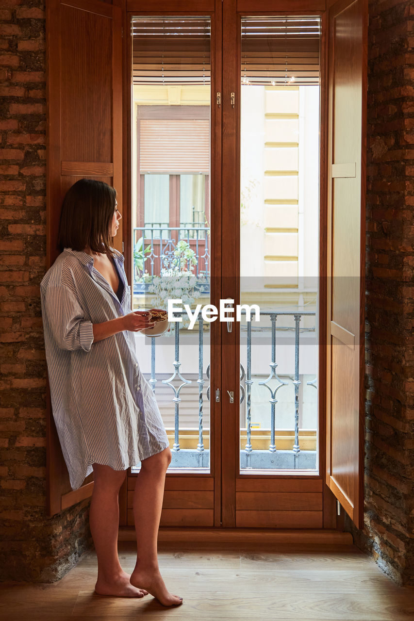 Young woman having breakfast next to a window at home.