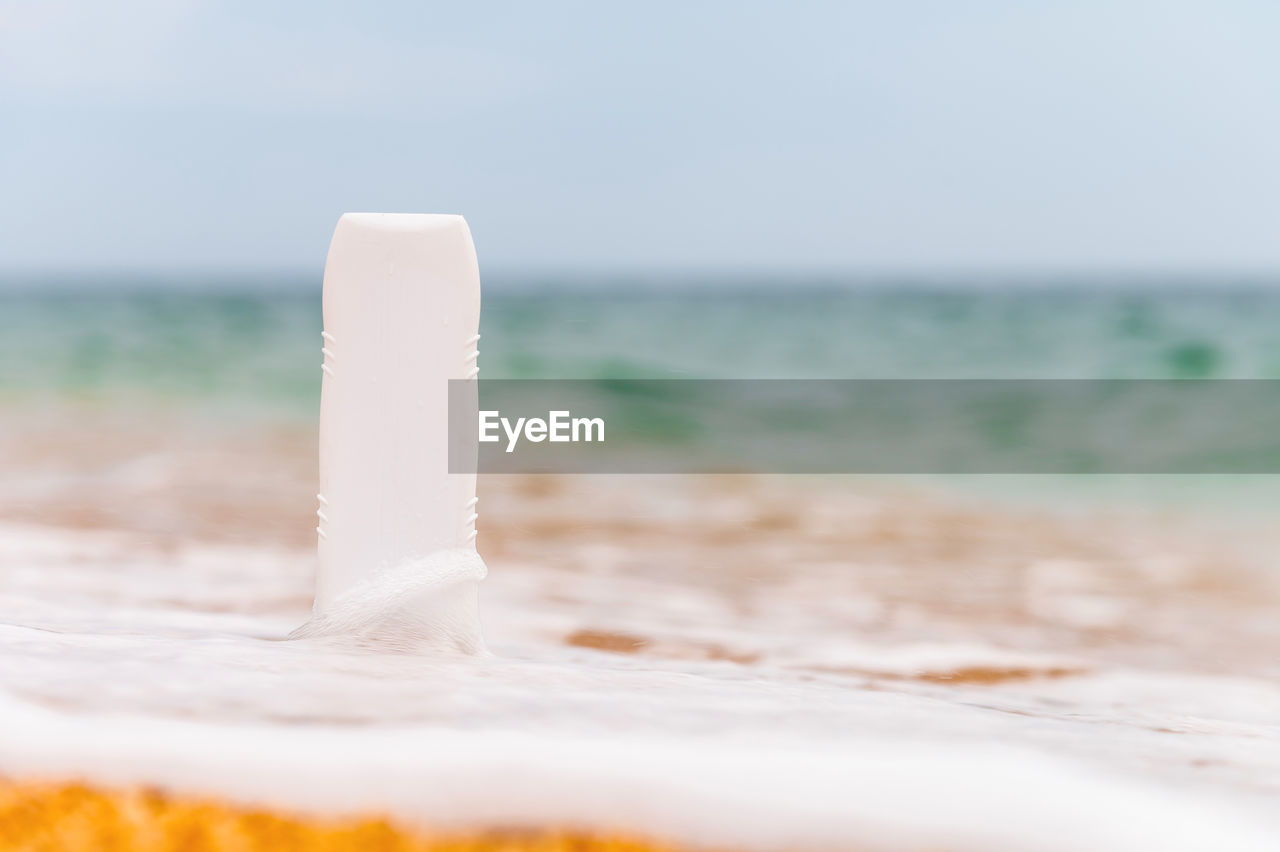 A bottle of sunscreen without a label on the beach on a sunny day. blank for advertising your cream