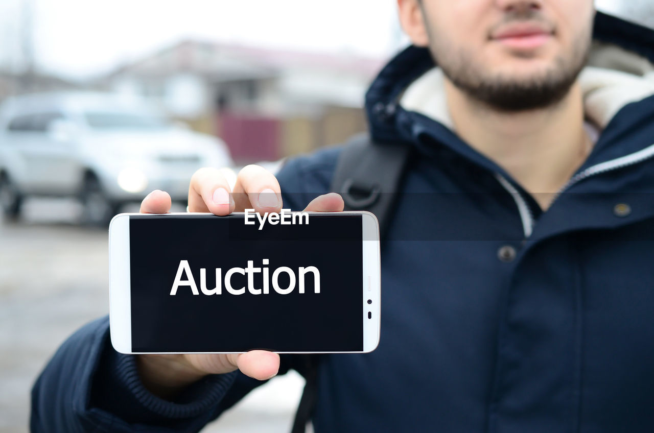 Man holding mobile phone with auction text