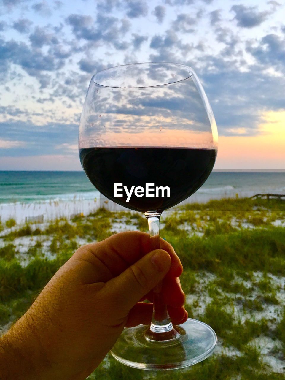 CLOSE-UP OF HAND HOLDING DRINK AGAINST SEA