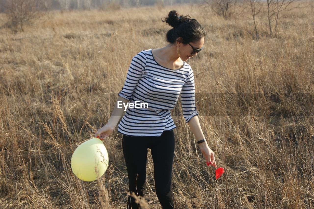 Young woman holding balloon standing on field