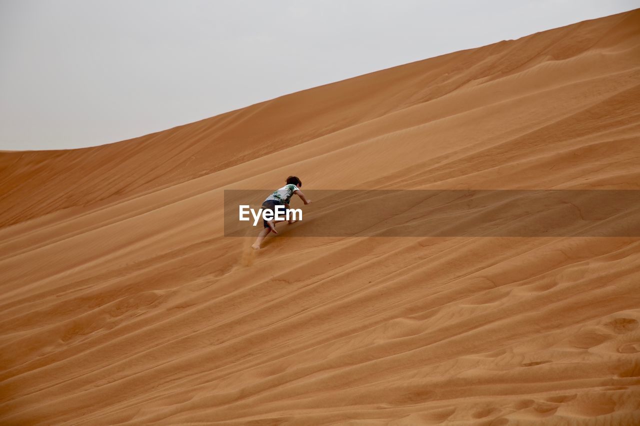 Low angle view of boy climbing on sand dunes at desert