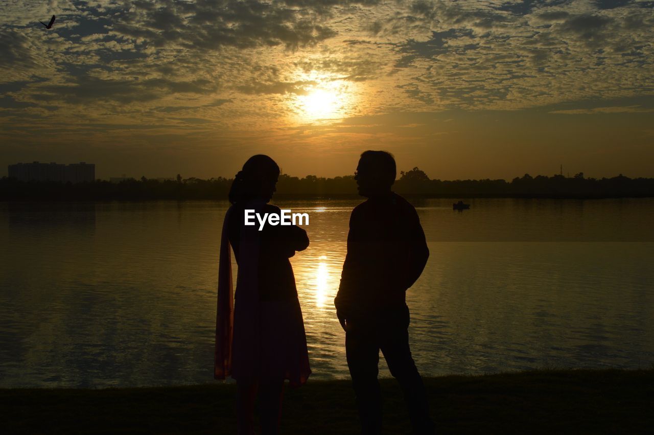 Silhouette friends standing on lake against sky during sunset