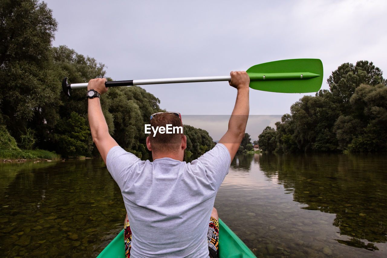 Rear view of man holding boat in lake against sky