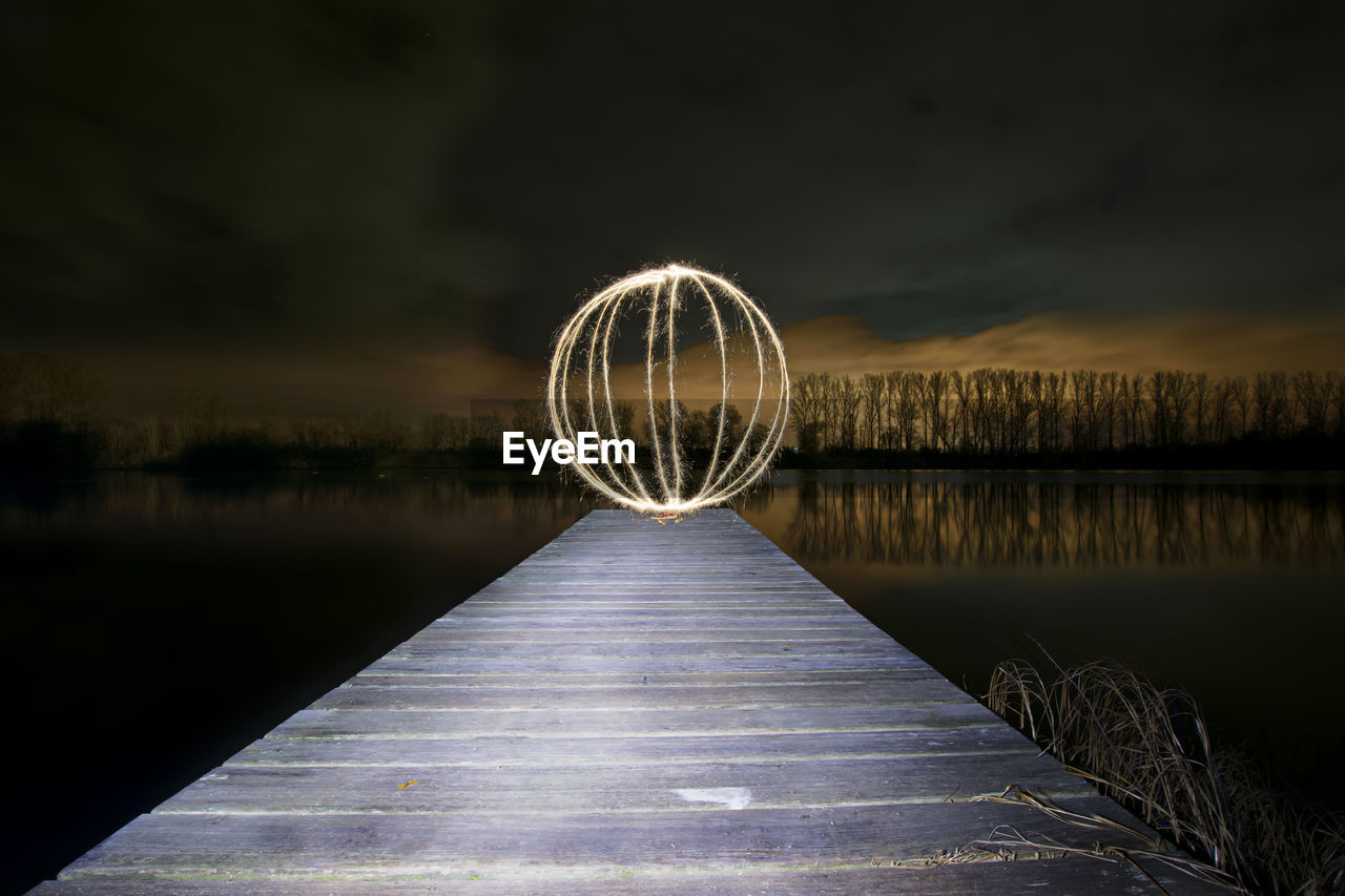 Ferris wheel by lake against sky at night