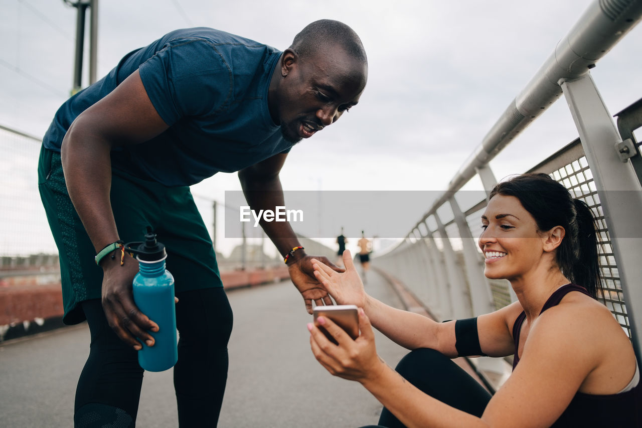 Female athlete smiling while showing mobile phone to sportsman on footbridge