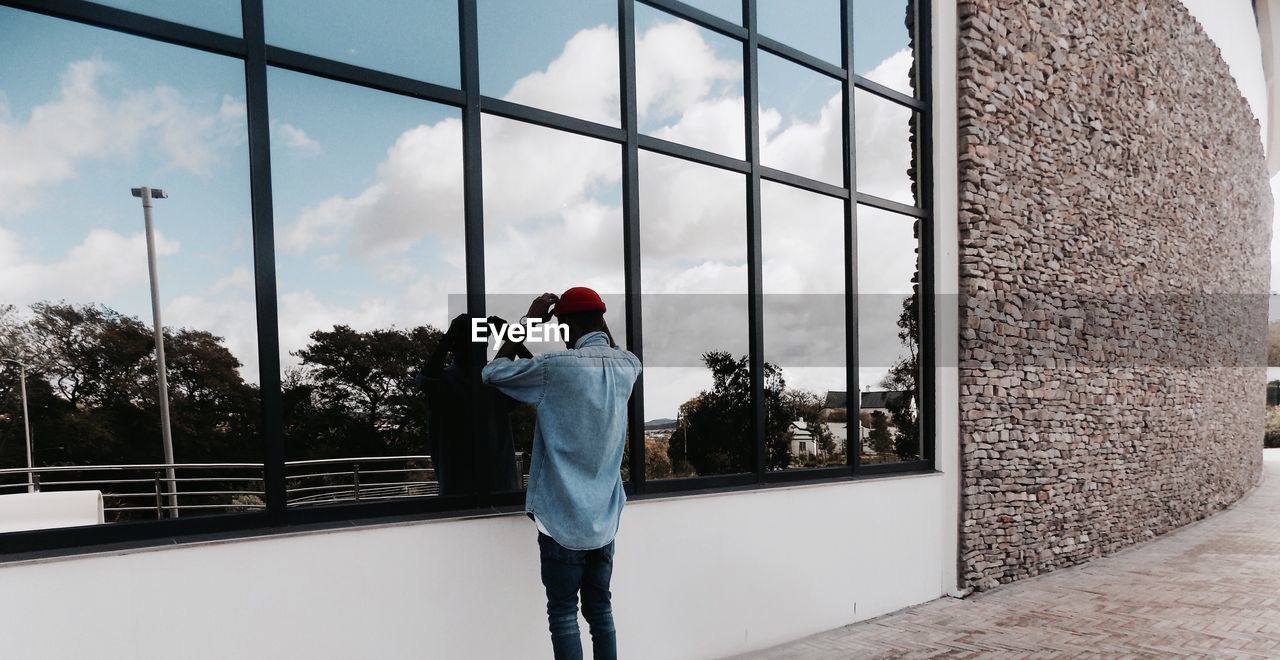 Reflection of man adjusting skull cap on modern building