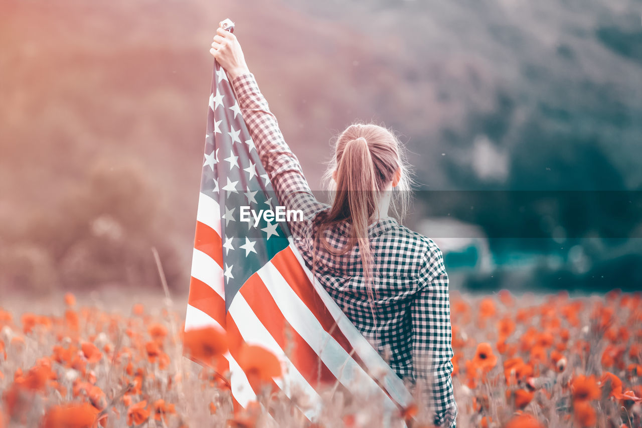 REAR VIEW OF WOMAN WITH UMBRELLA SITTING AGAINST FLAGS