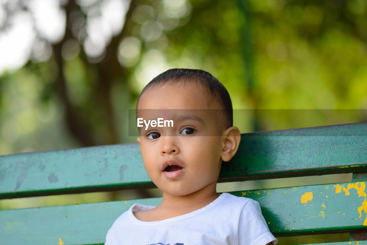 Close-up portrait of cute girl sitting on bench in park