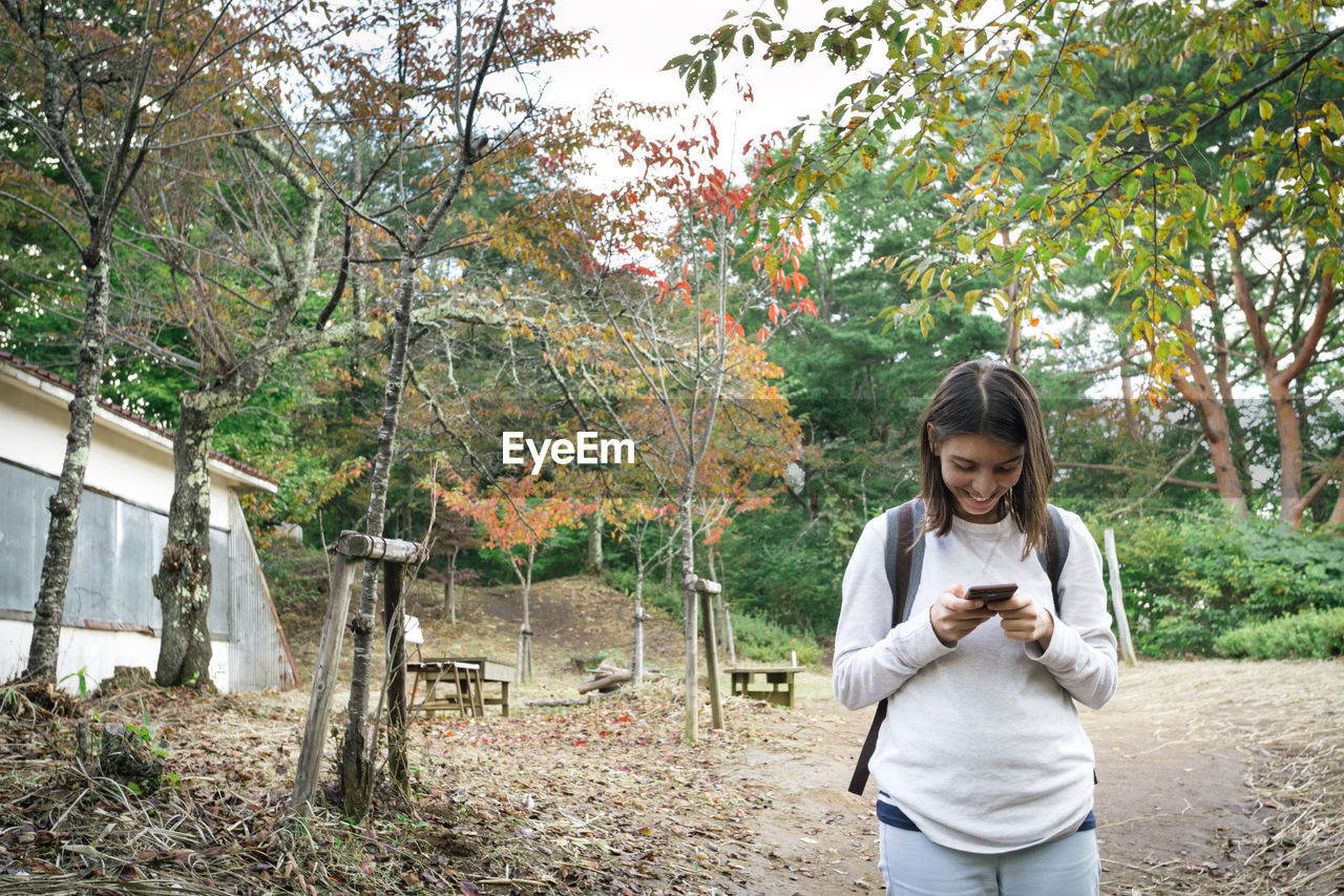 Woman using phone while standing against trees