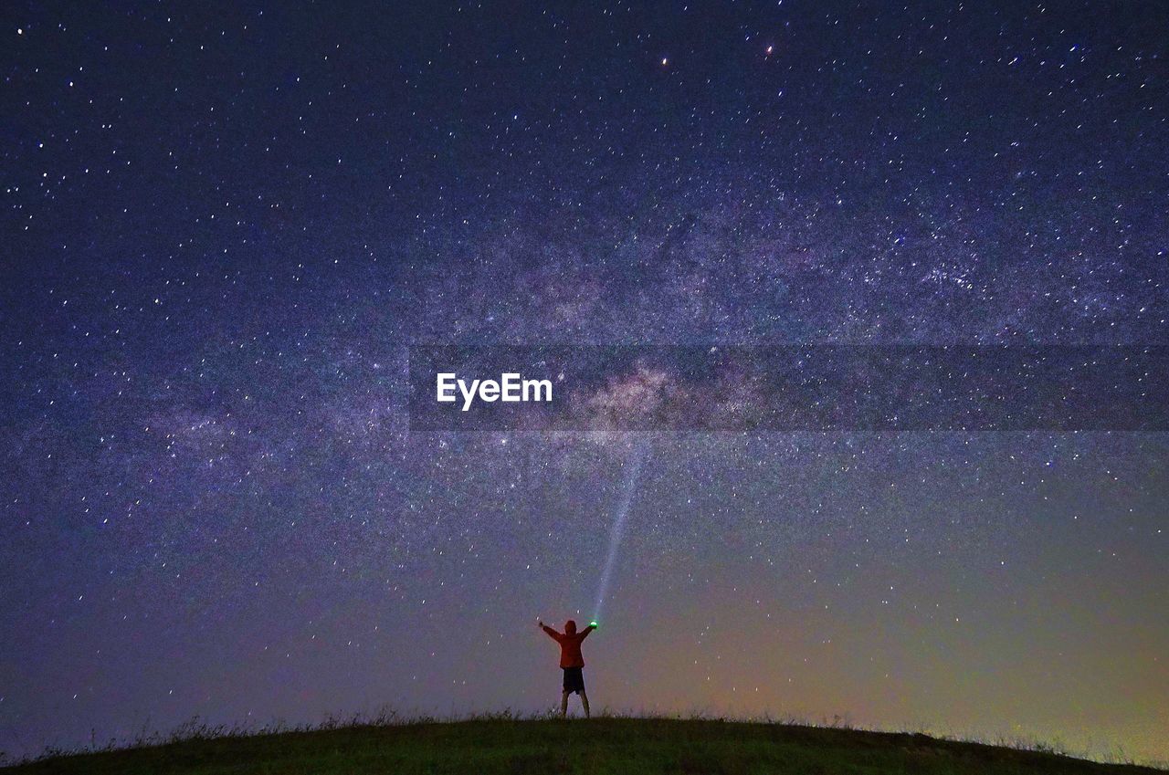 Rear view of man holding flash light while standing against star field at night