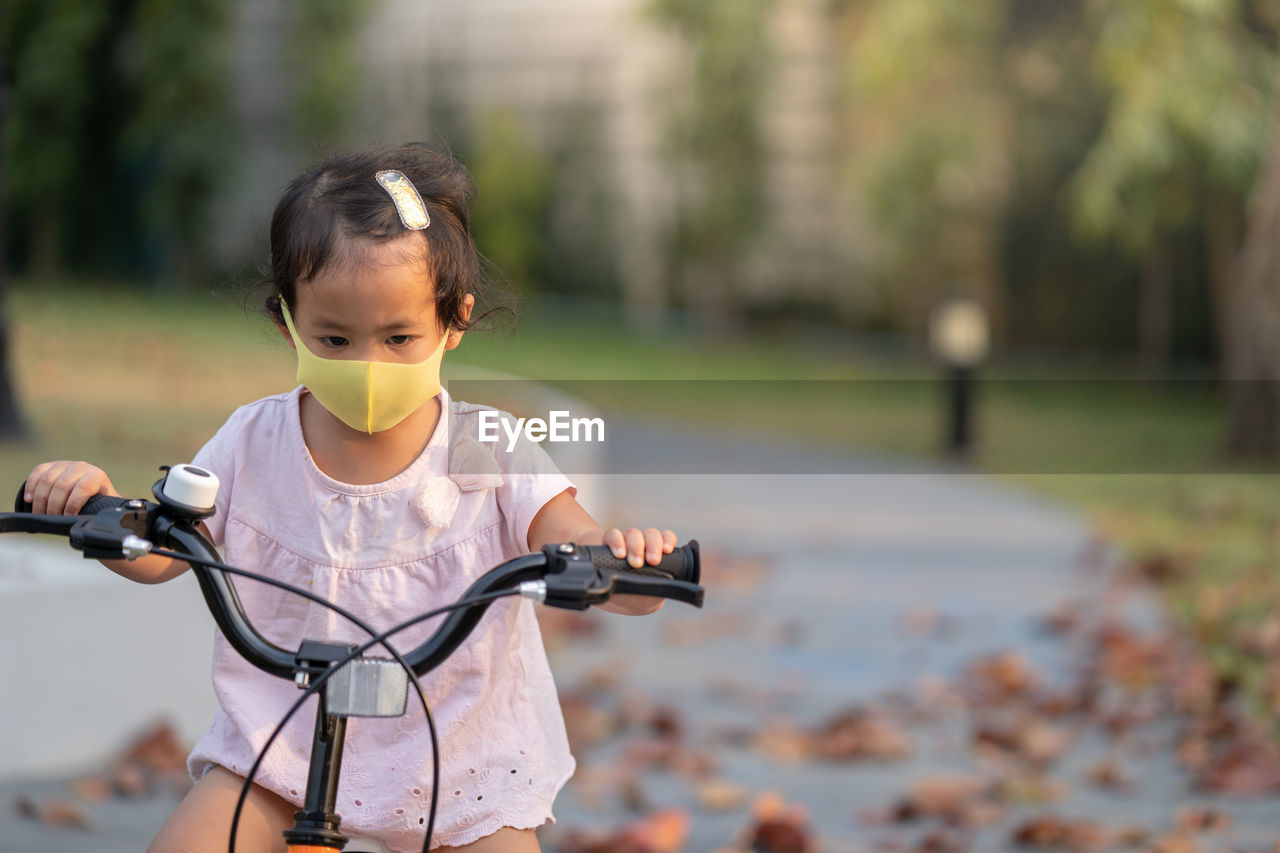 Little girl wearing anti pollution mask on her bike at park.