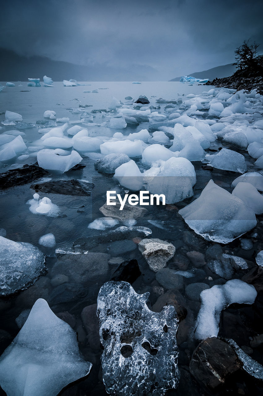 Ice on shore at beach during sunset