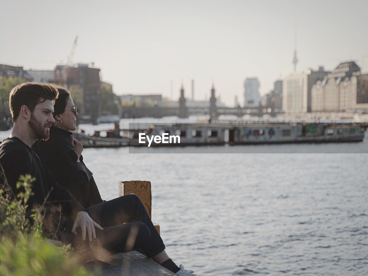 MEN SITTING BY RIVER IN CITY