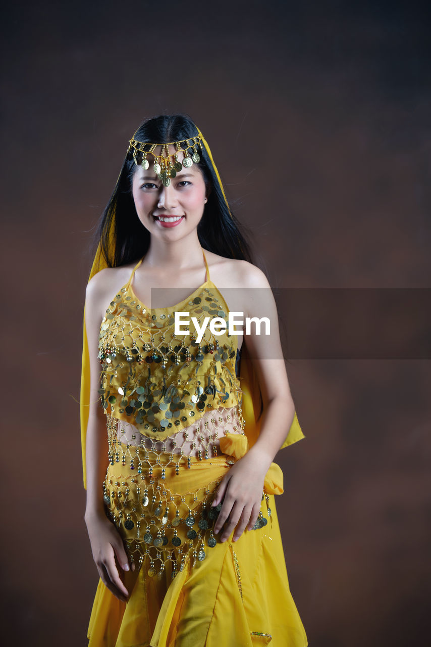 PORTRAIT OF A SMILING YOUNG WOMAN STANDING AGAINST YELLOW