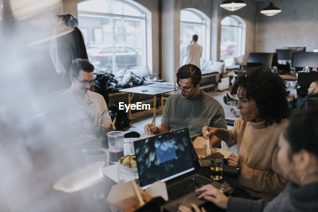 Businessman working while sitting amidst male and female colleagues at desk in creative office