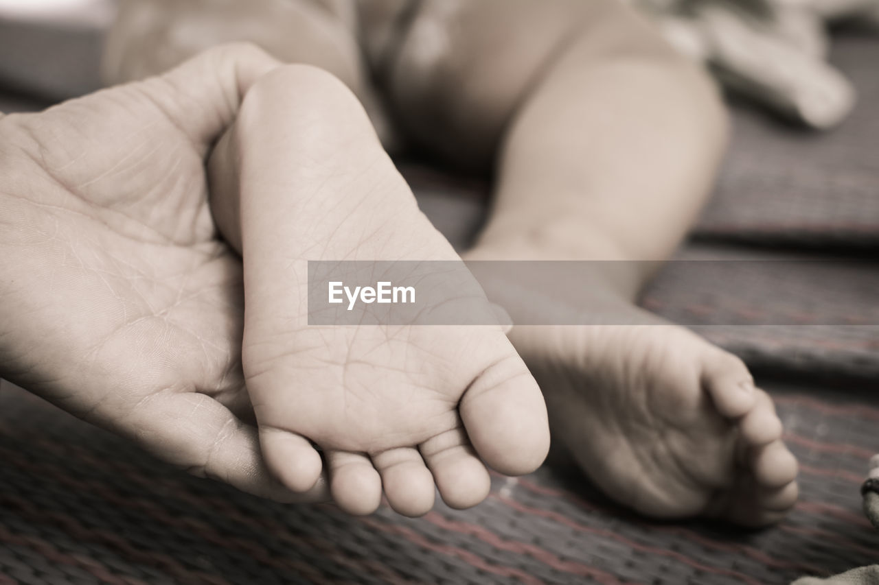 Cropped hand holding baby feet on bed