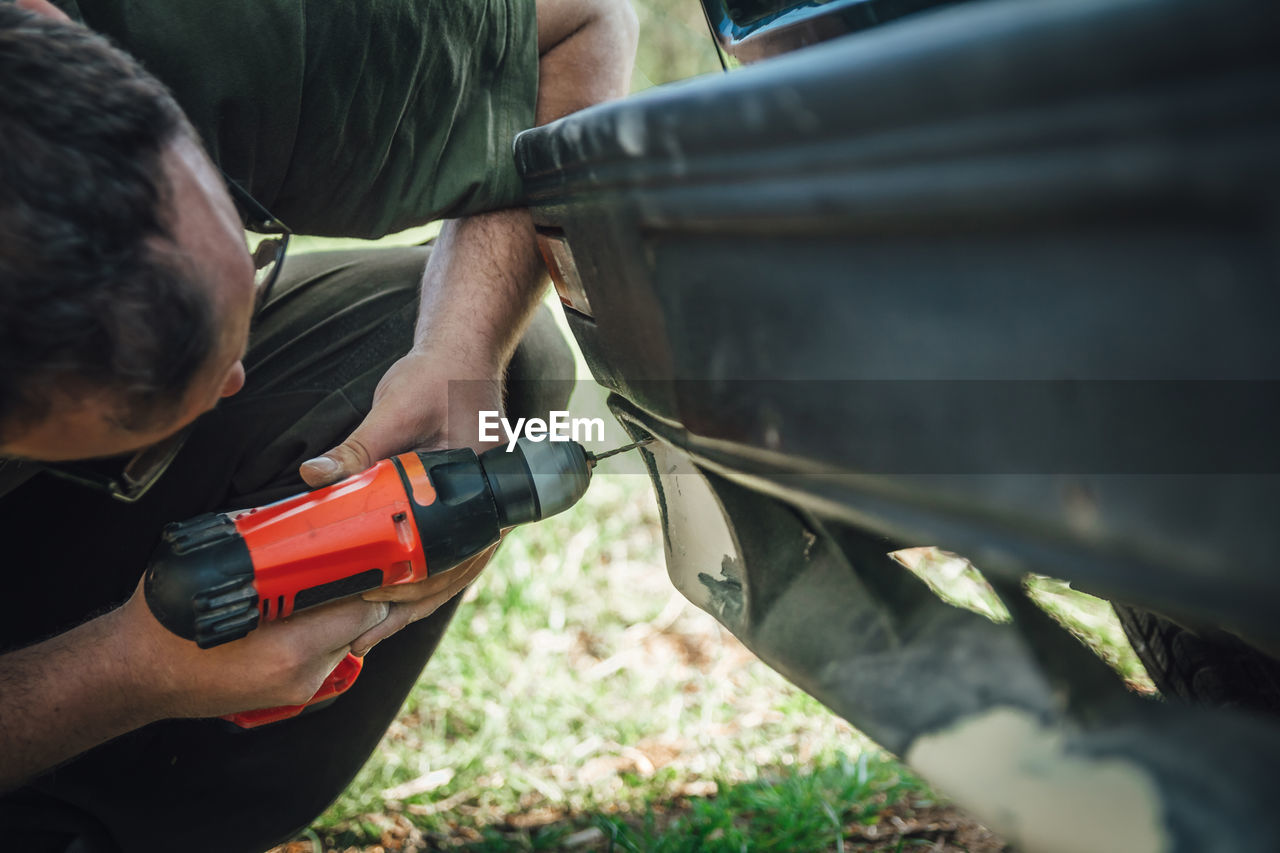 Young mechanic repairing a bumper on the car using a drill