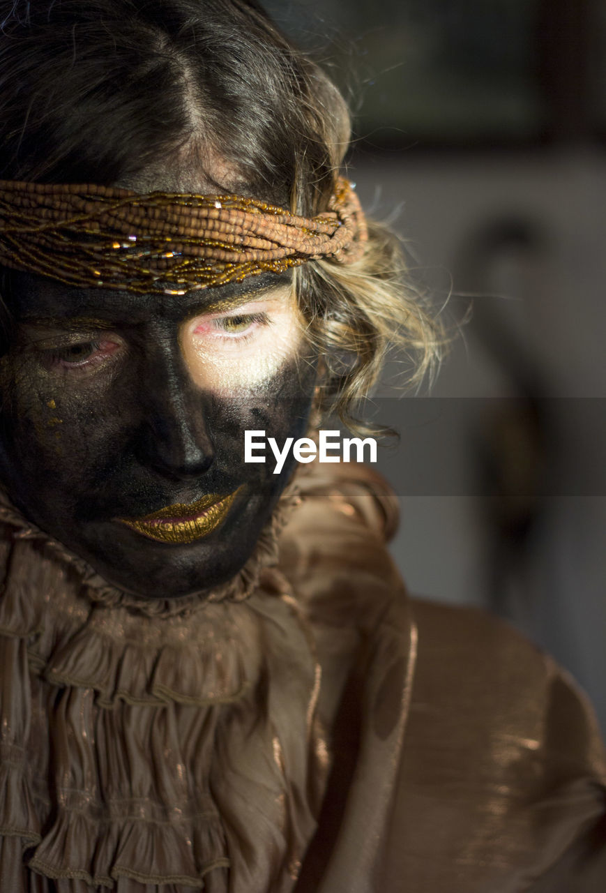 A woman with black painted face and golden clothes, party time, festival, close up portrait