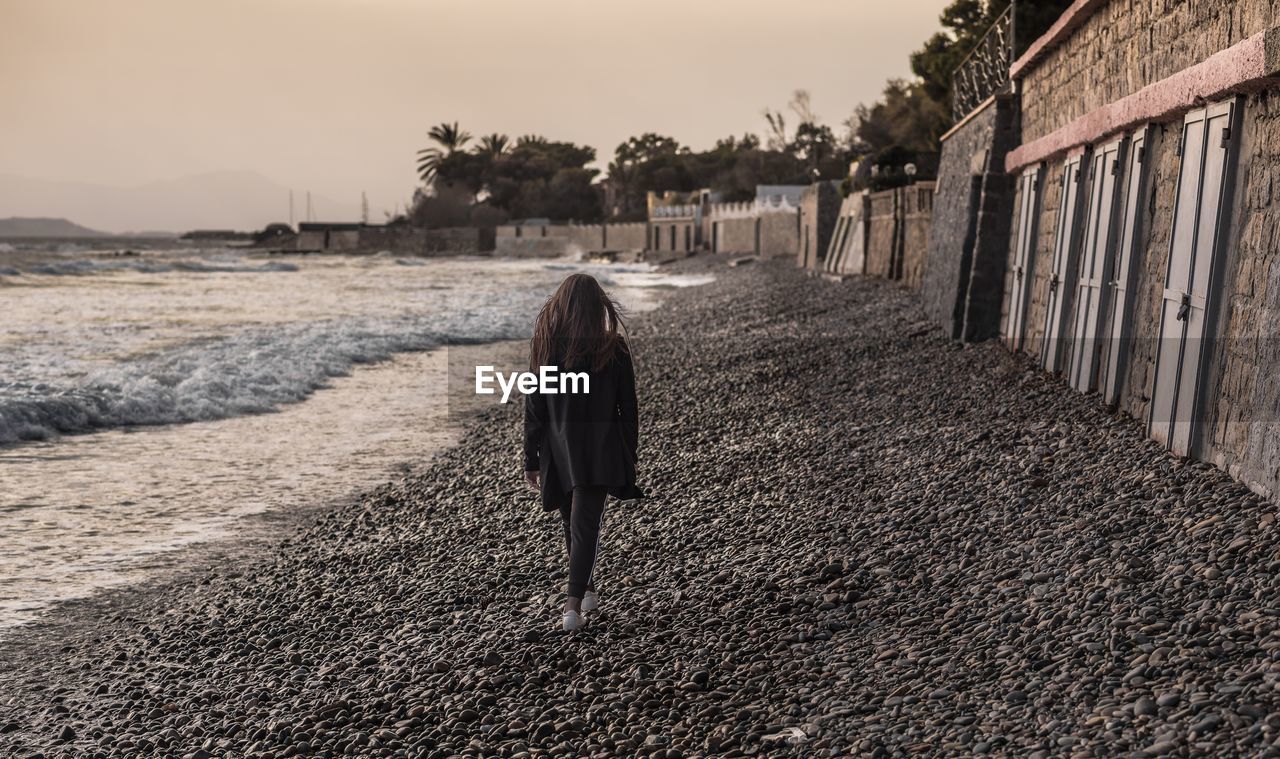 REAR VIEW OF WOMAN WALKING ON SANDY BEACH